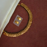 Antique Gold Plated Green Stone Lakshmi Coin Necklace Set with matching earrings on a maroon background.