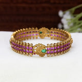 Antique Peacock Kemp and CZ Stone Bangle featuring rows of rectangular ruby red stones and small clear stones, with a central decorative motif and a green stone accent, displayed on a white surface.