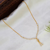 A delicate gold plated chain necklace with small white pearls, a CZ ball and a tassel charm, laid out on a soft white fabric background.