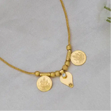 A delicate gold chain necklace with two coin-style pendants and a small thali charm, displayed on a soft white fabric surface.