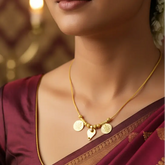 A woman wearing delicate gold plated chain necklace with two coin-style pendants and a small leaf thali charm.