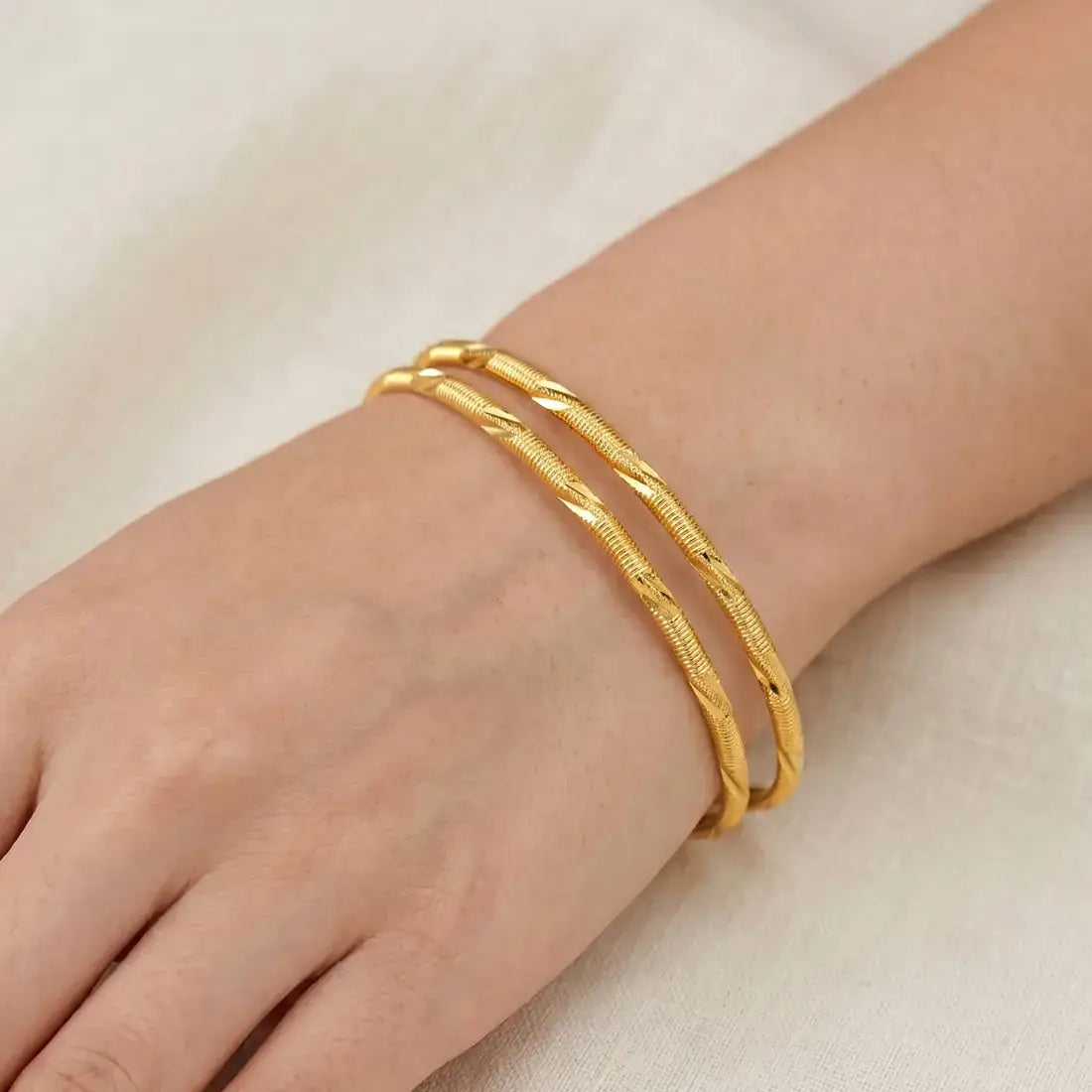 A hand wearing three Casual Gold Plated MC Mayoori Bangles with a textured surface.