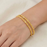 A hand wearing three Casual Gold Plated MC Mayoori Bangles with a textured surface.