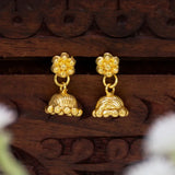 A pair of Cute Gold-Plated Kids Floral Jhumka Earrings with floral studs and bell-shaped dangling charms, displayed on a carved dark brown wooden surface.