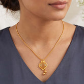 A close-up of a woman wearing a Gold-Plated Filigree Mesh Pendant Chain with a decorative pendant and small dangling beads, paired with a dark slate blue V-neck top.