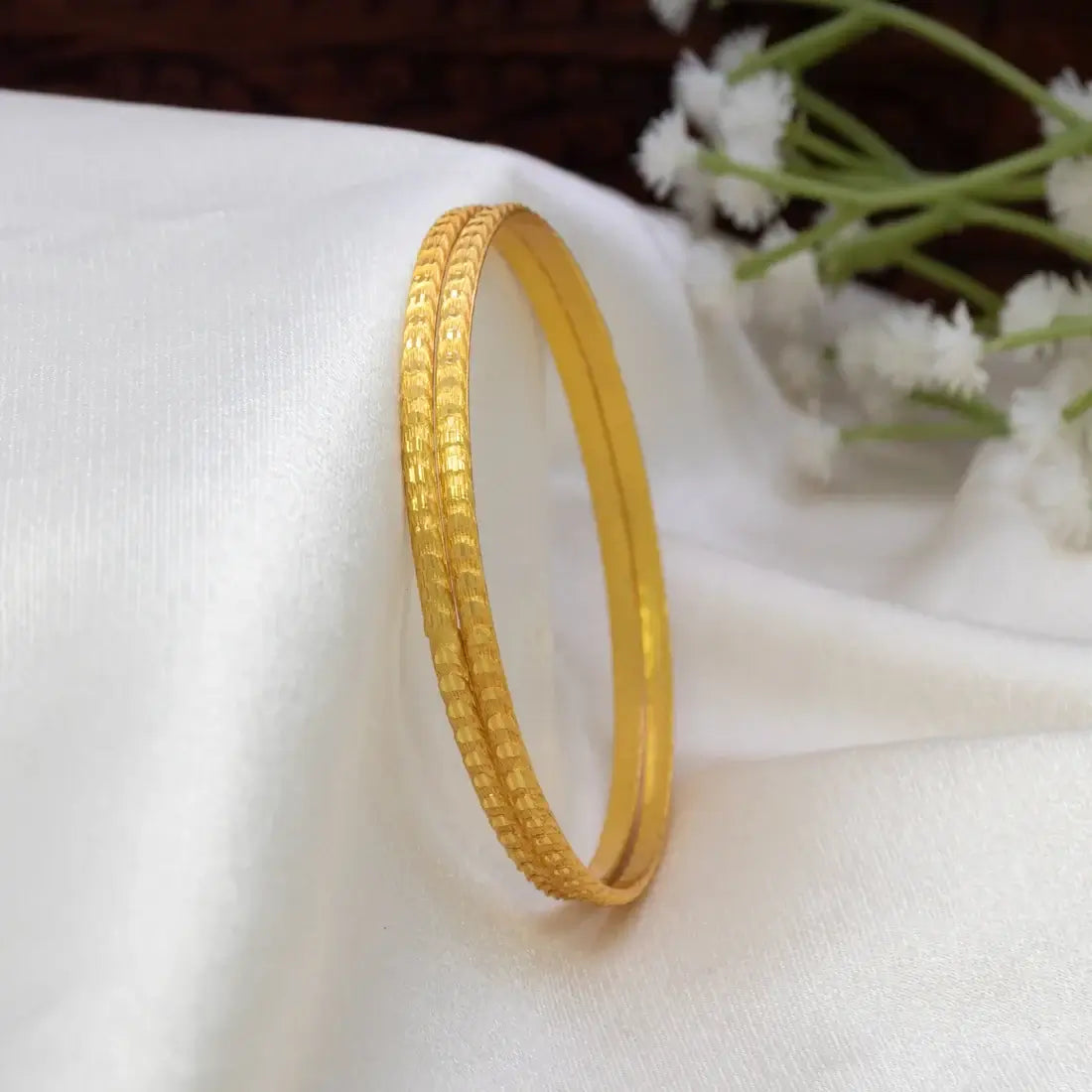 Gold-Plated Matte Designer Bangles with a textured surface, elegantly catching the light on a soft fabric background.