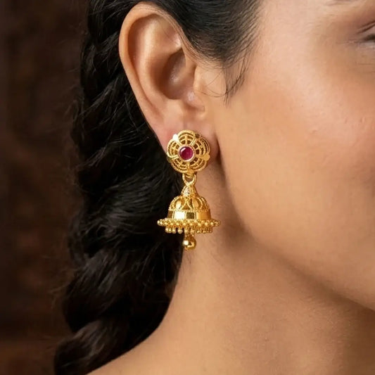 Small Gold Plated Ruby Stone Jhumka Earrings worn on a woman's ear, showcasing intricate design and ruby stone detail.