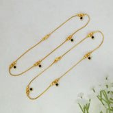 Gold-Plated Black Crystal Gold Bead Anklets with small black circular stones and decorative gold beads, arranged on a light textured background with white flowers in the corner.