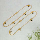 Gold-Plated Black Crystal Gold Bead Anklets with small black circular stones and decorative gold beads, arranged on a light textured background with white flowers in the corner.