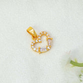 A Gold-Plated CZ Heart Pendant Charm with clear round and baguette-cut crystals, resting on a textured white fabric background with a small white flower prop.