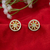A pair of Gold-Plated CZ Sunburst Stud Earrings with circular floral designs set with clear stones, displayed on a textured red fabric background with small white flowers in the upper corner.