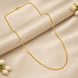 A delicate Gold-Plated Curb Link White Pearl Chain with small white pearl beads spaced along the chain, displayed on a draped beige satin fabric with white flowers in the corners.