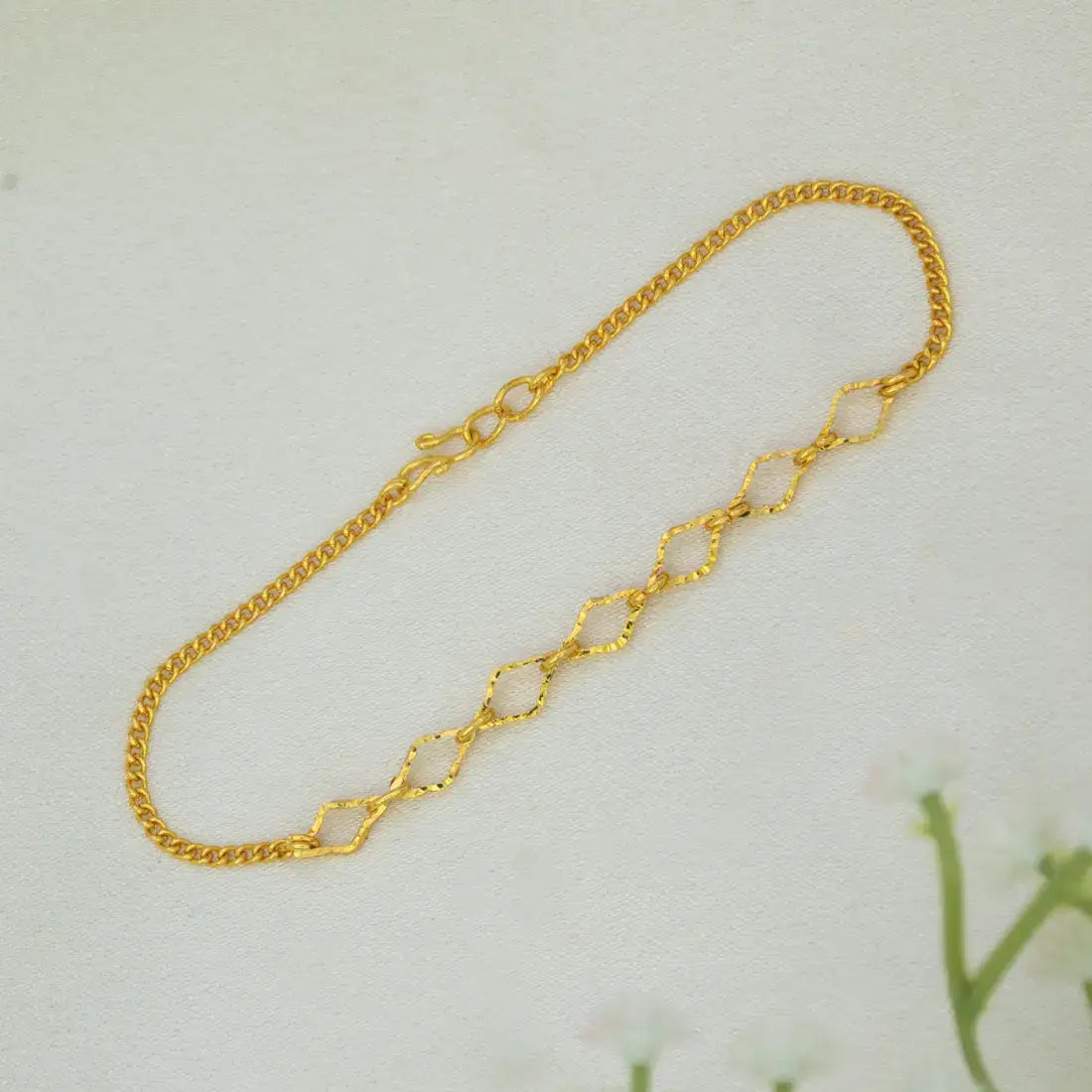 A delicate Gold-Plated Designer Chain Bracelet for Girls with elongated, textured oval links, displayed on a light off-white textured surface.