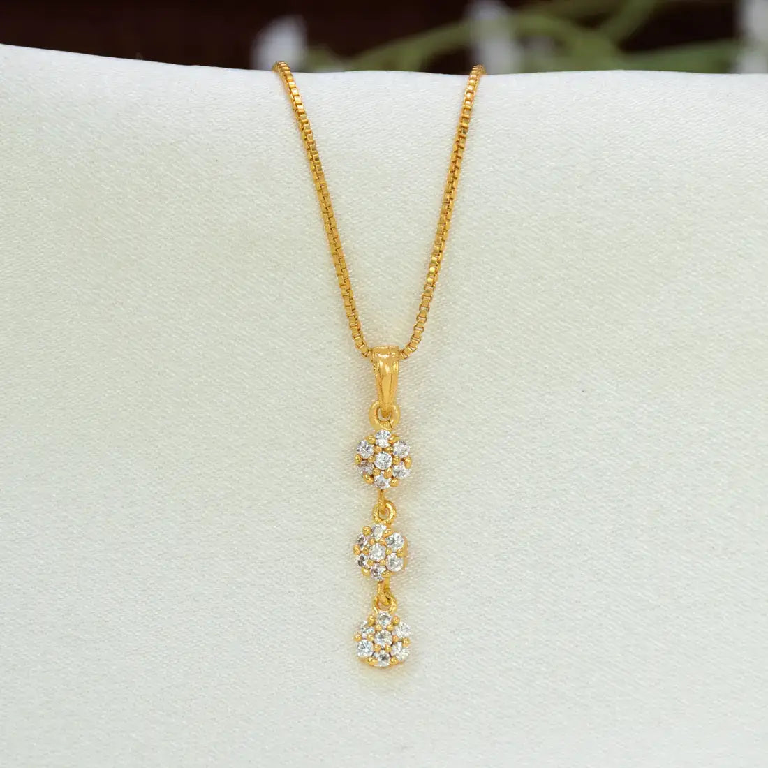 A gold chain necklace with a vertical Gold-Plated Three-tier Stone Floral Drop Pendant featuring three small flower clusters of cz stones, displayed on a white jewelry stand.