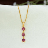 A gold chain necklace with a vertical Gold-Plated Three-tier Stone Floral Drop Pendant featuring three small flower clusters in deep ruby-red gemstones, displayed on a white jewelry bust.
