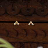 A pair of Gold-Plated Triple CZ Stone Second Stud Earrings with clear gemstones, displayed on a carved dark brown wooden surface.