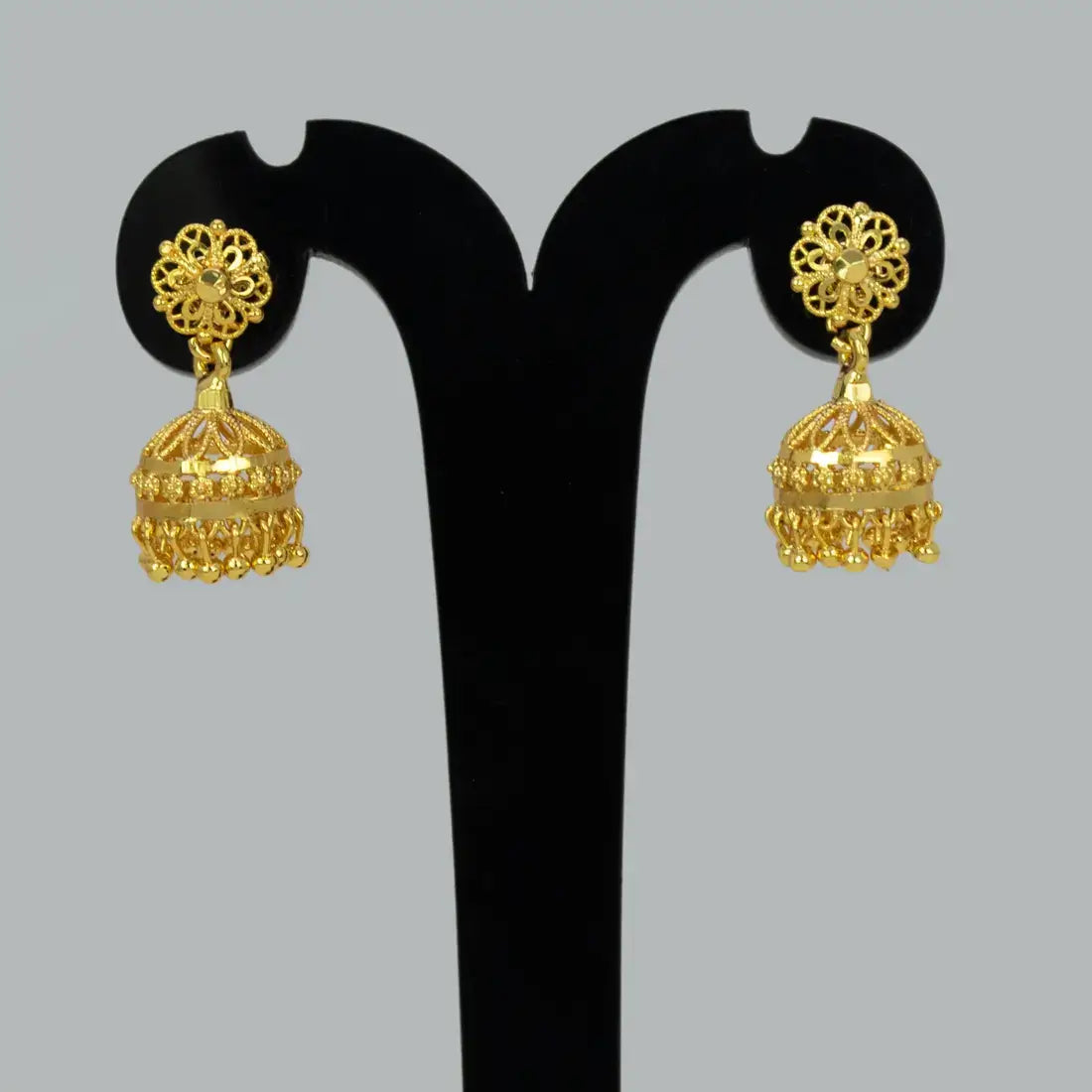 Pair of gold earrings on a black stand against a gray background