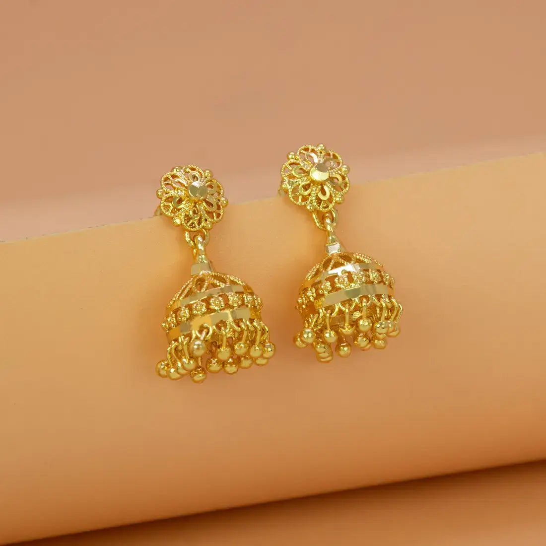 Gold earrings on a beige arm with a beige background