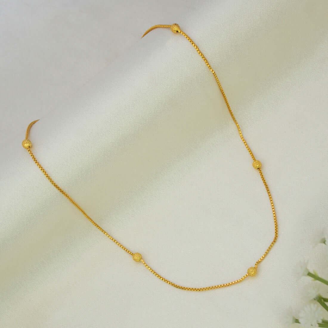 A delicate Gold Plated Beaded Box Chain for Babies with small, evenly spaced textured gold beads, displayed on a soft, draped white fabric background.