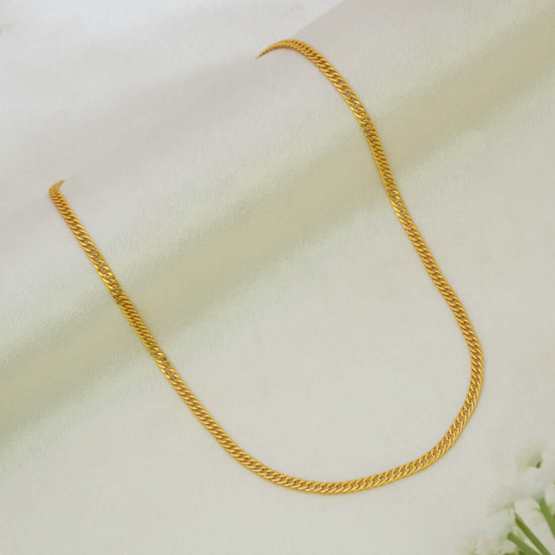 A Gold Plated Flat Curb Link Baby Chain displayed in a U-shape on a soft, off-white textured fabric background.