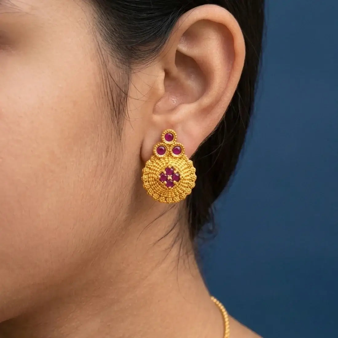 Gold Plated Floral Stone Studded Stud Earrings worn in a model's ear, featuring ruby stones and a textured gold finish.