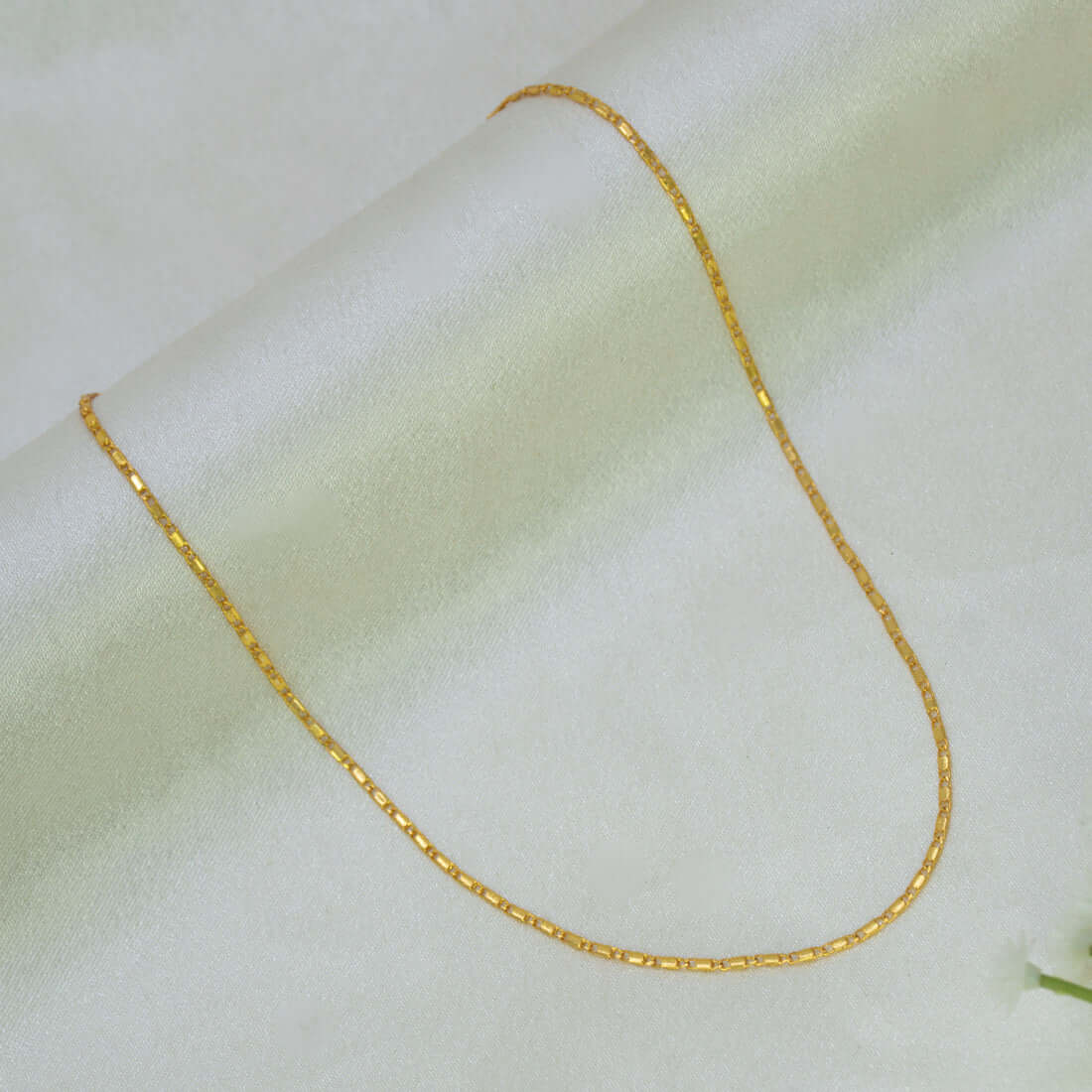 A Gold Plated Thin Titanic Chain for Kids necklace draped in a U-shape over a soft, light-colored fabric background.