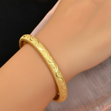 a gold-plated bangle bracelet with an intricate wave pattern design.