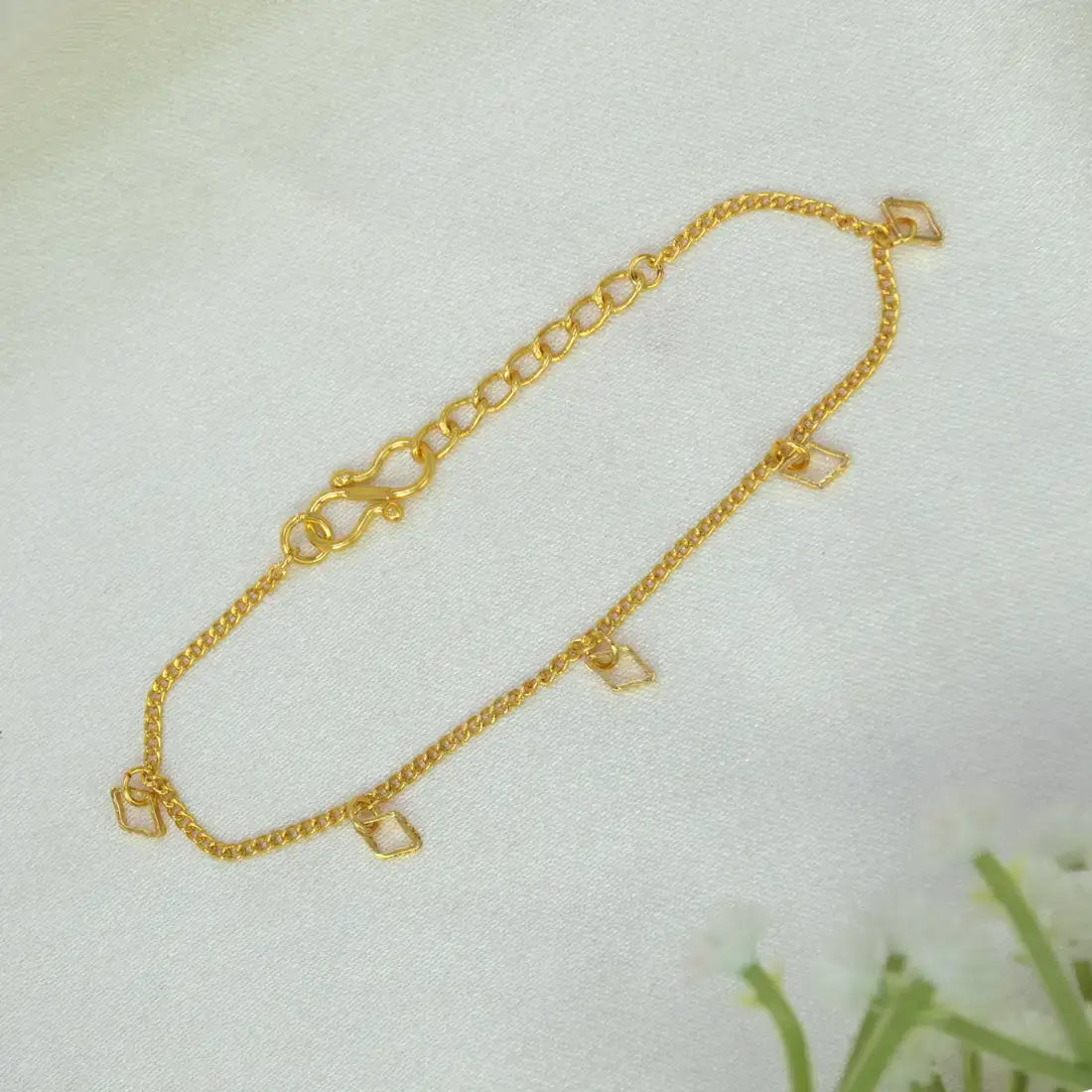 A delicate Gold plated geometric charm hanging bracelet, displayed on a soft white textured fabric background.