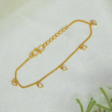 A delicate Gold plated geometric charm hanging bracelet, displayed on a soft white textured fabric background.