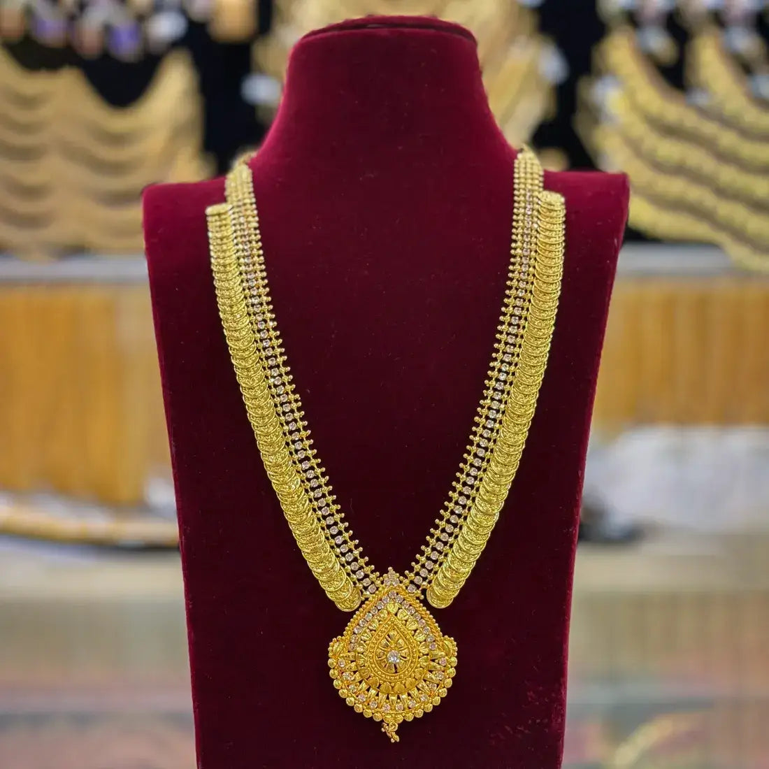 Gold-Plated Stone Lakshmi Kasu Haram Necklace displayed on a velvet bust with intricate design and teardrop pendant.