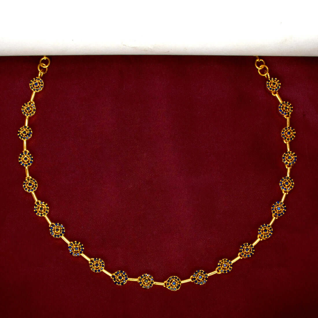 Marvelous Gold Plated Round Stone Necklace displayed against a maroon background, showcasing its dazzling design.