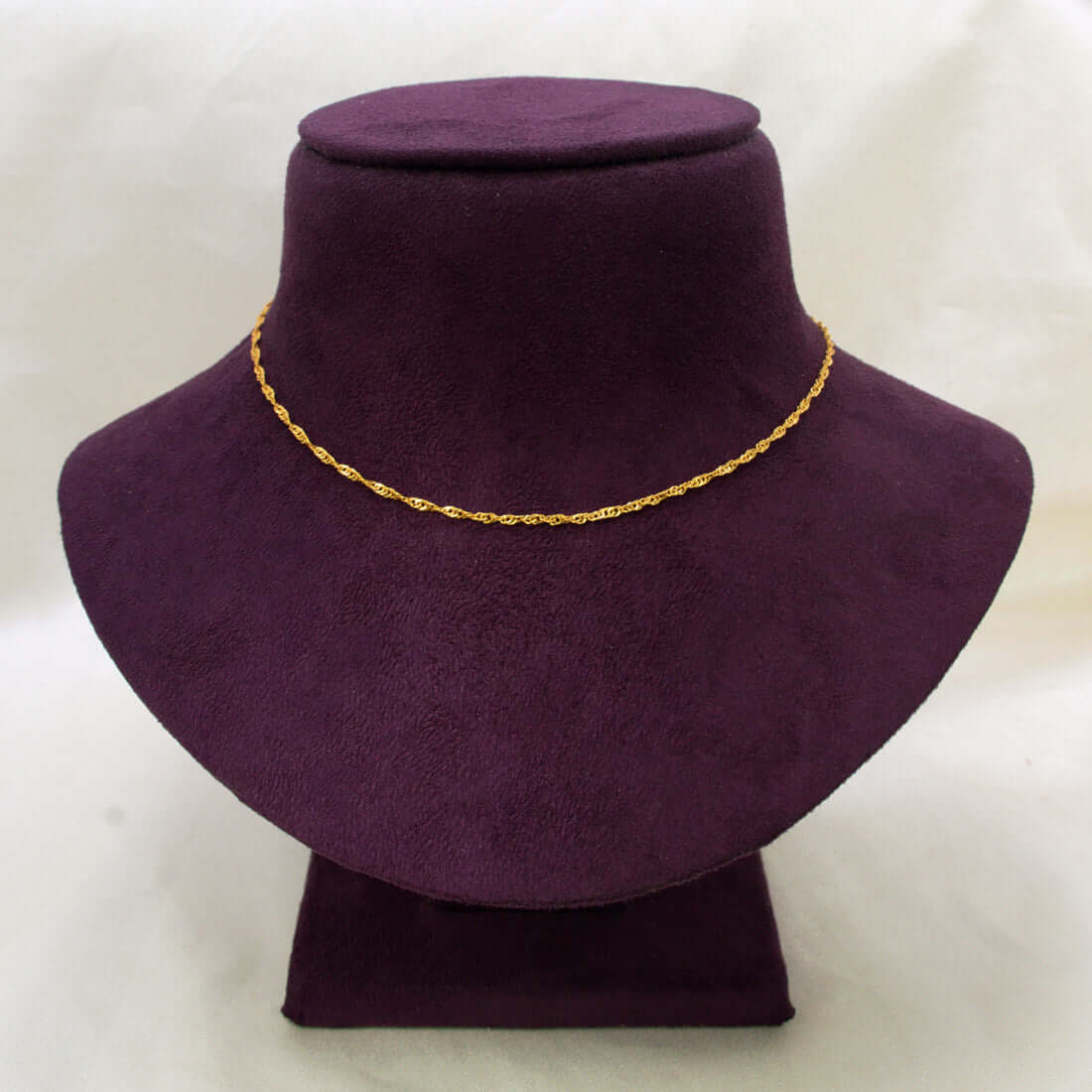 A delicate Popular Gold-Plated Twisted Singapore Chain displayed on a dark purple velvet jewelry bust against a light off-white background.