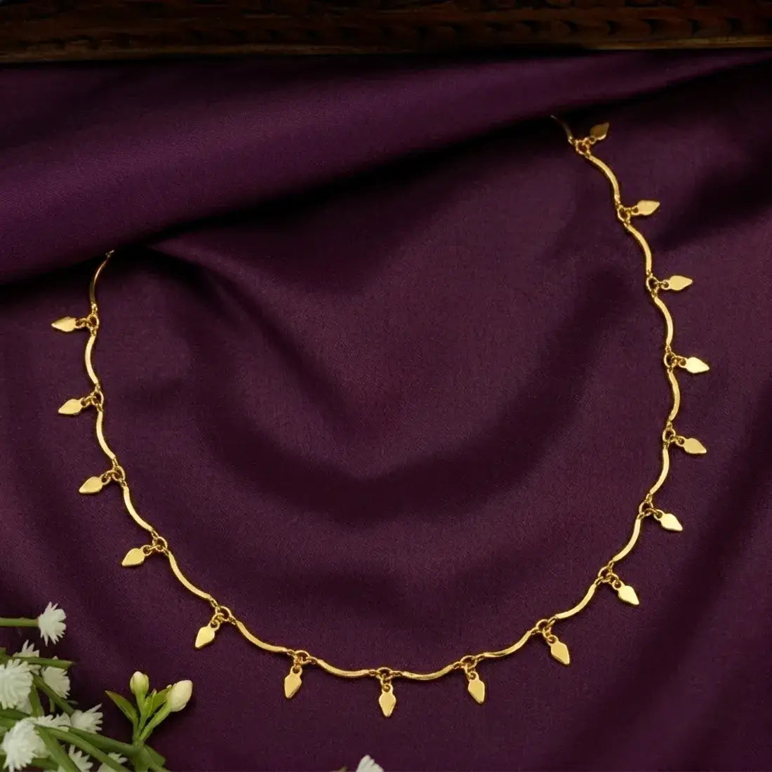 Gold Plated Wavy Chain Elakkathali Necklace displayed on purple fabric with delicate leaf-shaped charms.