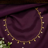 Gold Plated Wavy Chain Elakkathali Necklace displayed on purple fabric with delicate leaf-shaped charms.