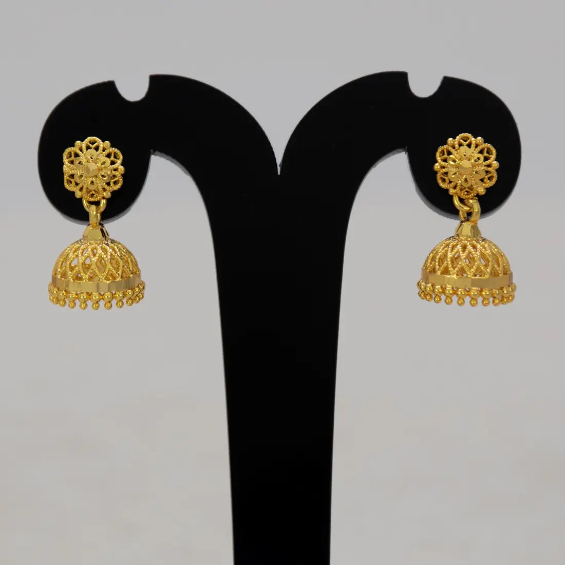 Gold-plated earrings on a black earring stand against a gray background