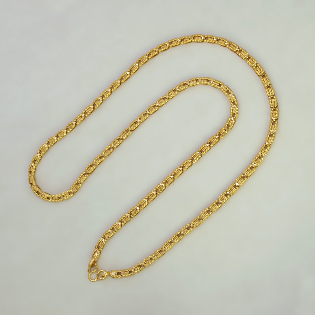 A gold-colored chain necklace with a textured, woven link design, displayed on a plain light gray background.
