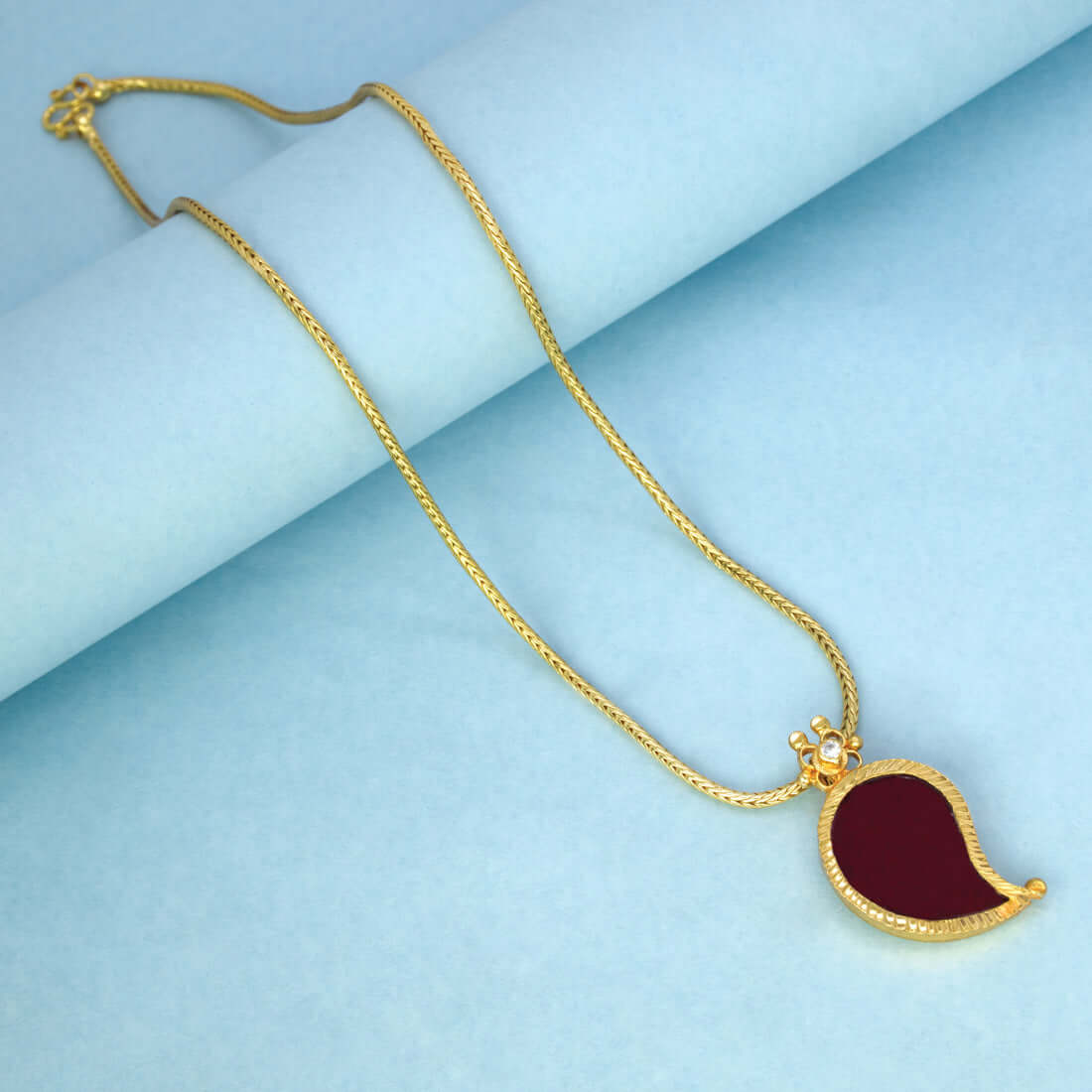 Traditional Gold-Plated Mango Pendant Chain with dark red CZ stone on a gold chain against a blue background.