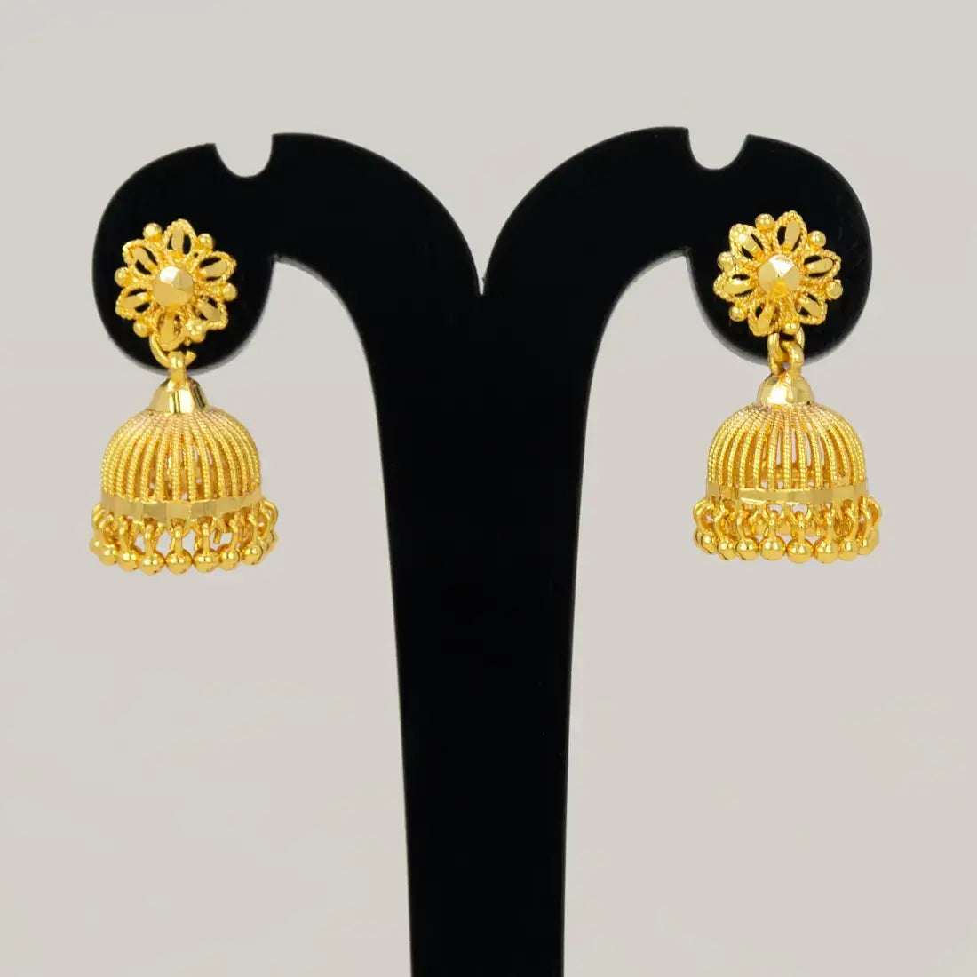 Pair of gold earrings on a black stand against a light gray background
