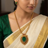 A woman wearing a traditional Indian outfit in a green and ivory saree, showcasing a Antique Kerala Traditional Teardrop Pendant Necklace Set and matching green earrings.