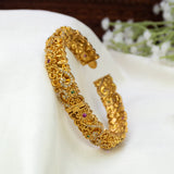 An Antique Floral Multi-colour Stone Cuff Bangle with small inset stones and tiny colored gem accents, displayed on a white fabric surface with blurred white flowers in the background.
