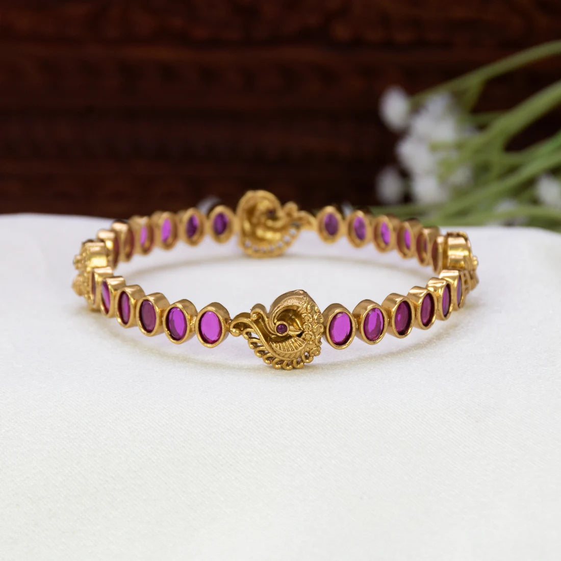 Antique gold plated ruby stone peacock bangle with oval ruby-red stones and detailed peacock motifs on a traditional South Indian temple bangle