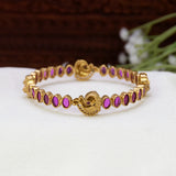 Antique gold plated ruby stone peacock bangle with oval ruby-red stones and detailed peacock motifs on a traditional South Indian temple bangle
