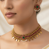 A close-up of a model wearing an ornate Antique Kemp Elakkathali Choker Necklace Set, decorated with green stones, pinkish-red stones, and white pearl-like accents.