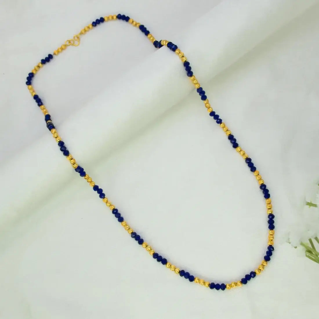 A Blue Crystal and Golden Bead Chain for Women featuring alternating dark blue and gold beads, displayed on a soft white fabric background.