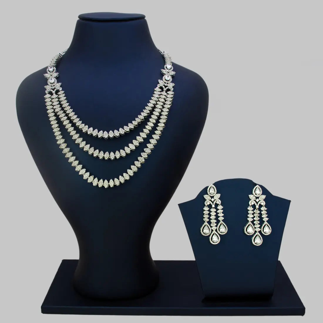Rhodium-plated American Diamond necklace and earrings set on black mannequin stands against a gray background