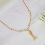 A delicate gold-plated curb chain necklace with small white pearls and a tassel charm, laid out on a soft white fabric background.