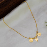 A delicate gold plated chain necklace with two coin-style pendants and a small leaf charm, displayed on a soft white fabric surface.