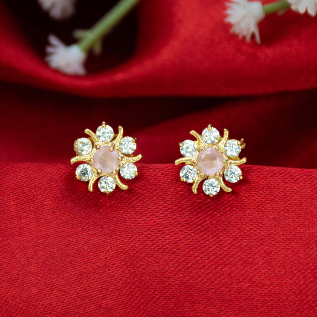 Gold Plated Pastel Central Stone CZ Flower Studs with pastel pink center and sparkling stones on red fabric.