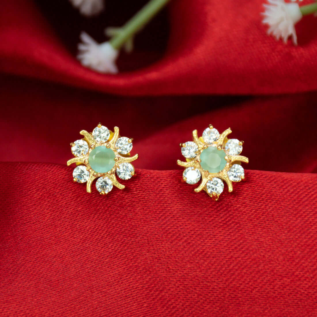 Gold Plated Pastel Central Stone CZ Flower Studs with mint green stone on red background.