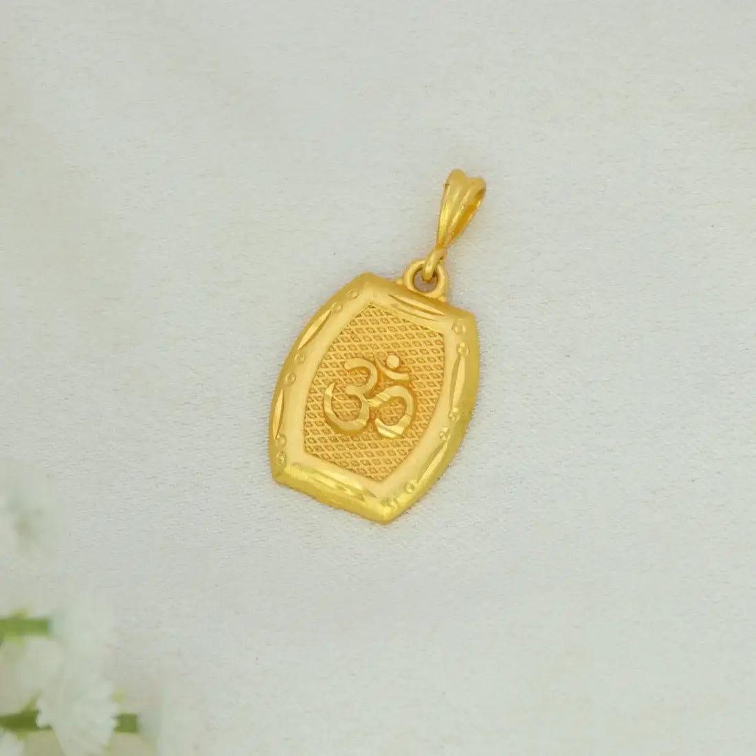 Devotional Unisex Gold Plated Rectangle Om Pendant charm featuring an Om symbol in the center, displayed on a textured off-white background with small white flowers in the corner.